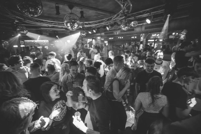 Menschen tanzen und feiern in einem lebhaften Nachtclub mit Licht- und Geräuscheffekten.