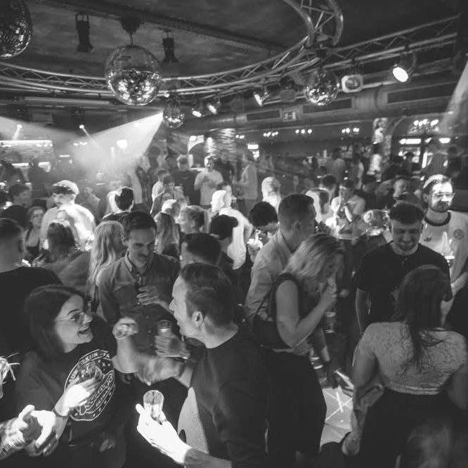 Menschen tanzen und feiern in einer belebten Disco mit Lichtern und Musik von DJ Driessen.