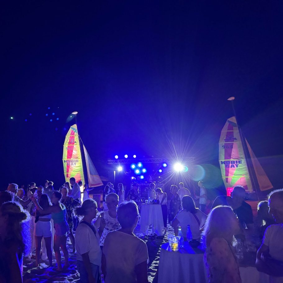 Nachtveranstaltung am Strand mit bunten Lichtern und der Menschenmenge. DJ Driessen legt auf einer Bühne zwischen zwei Hoobie Cat auf.