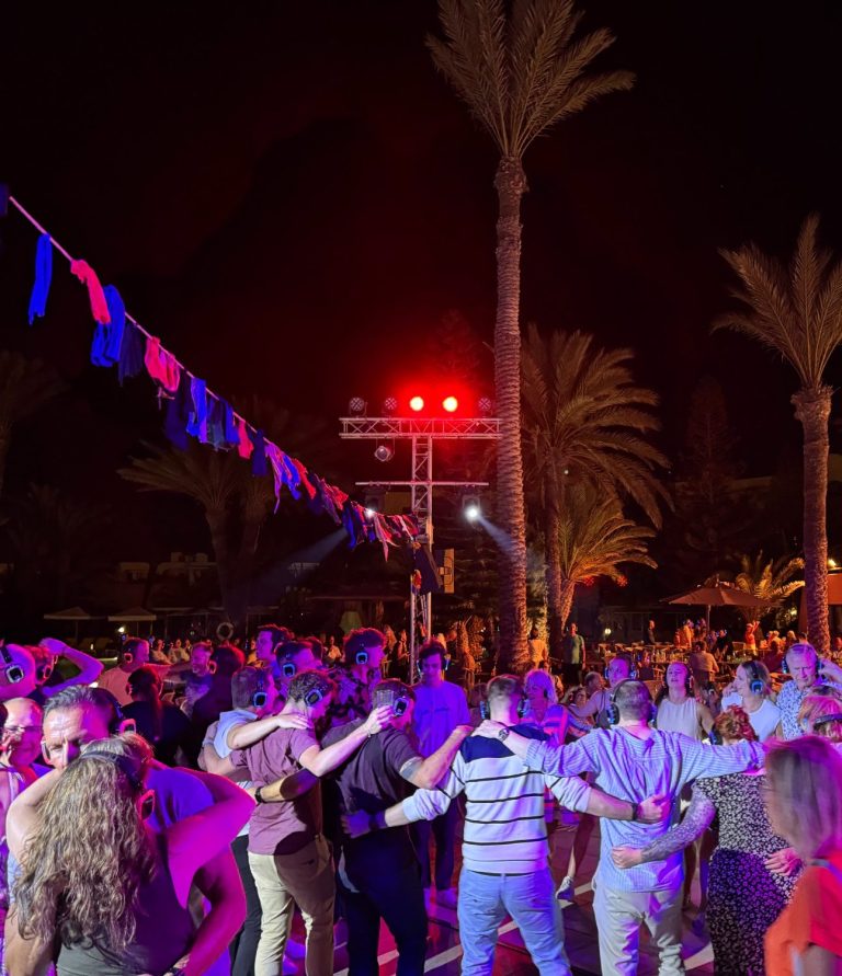 Bunte Menschen feiern eine Kopfhörerparty / Silent-Night  unter Palmen bei Nacht mit Lichtern und Musik.