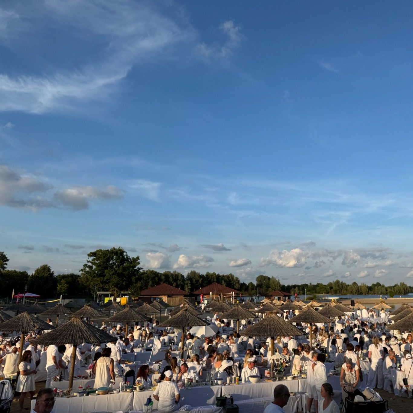 Große Menschenmenge in weißer Kleidung bei einem Event im Freien, blauer Himmel.