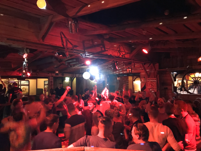 Menschenmenge tanzt und feiert in einer lebhaften Bar mit rotem Licht und Disco-Kugel.