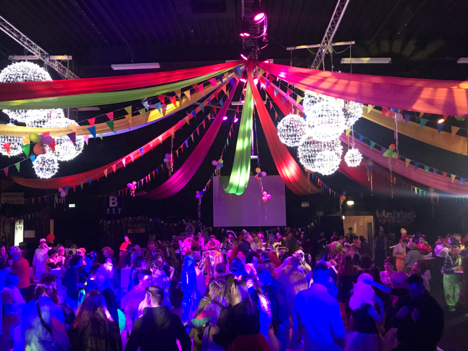 Bunte Dekoration mit Lichtern und verstreuten Farbbanden über tanzender Menge.
