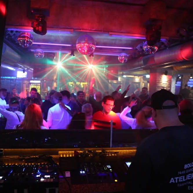 Eine Menschenmenge tanzt in einem beleuchteten Club mit DJ Driessen und farbigen Lichtern.
