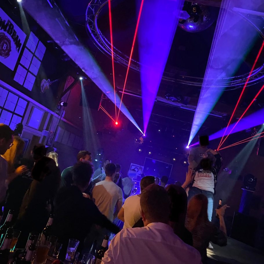Bunte Lichter und Laserstrahlen beleuchten eine belebte Clubszene.