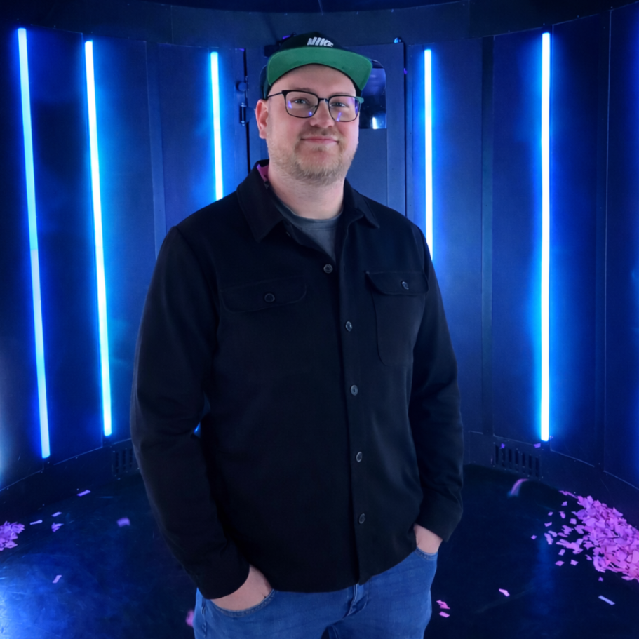 DJ Driessen in schwarzer Jacke steht vor blauen Lichtstrahlen und pinken Konfetti.