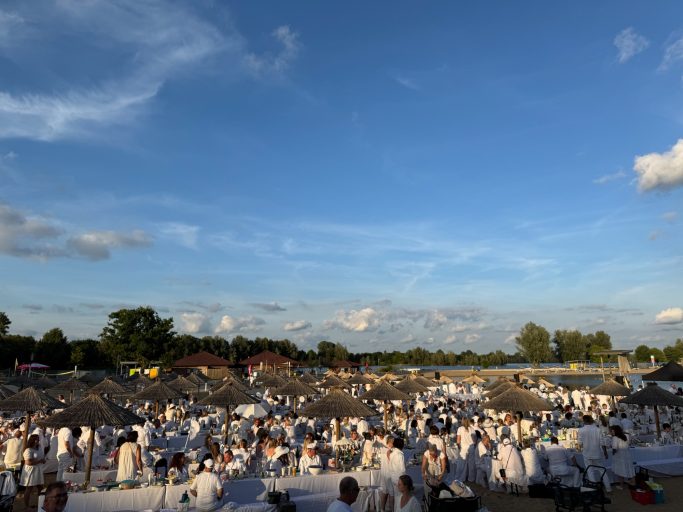 Menschen in weißer Kleidung versammeln sich unter blauem Himmel mit Wolken.