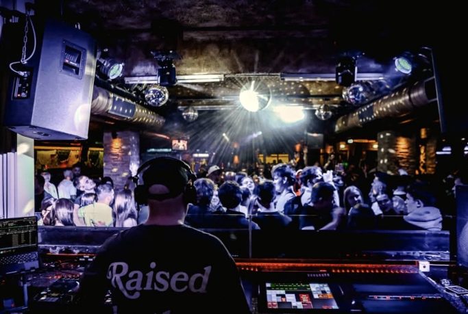 DJ an einem Mixer mit Publikum in einem beleuchteten Club.