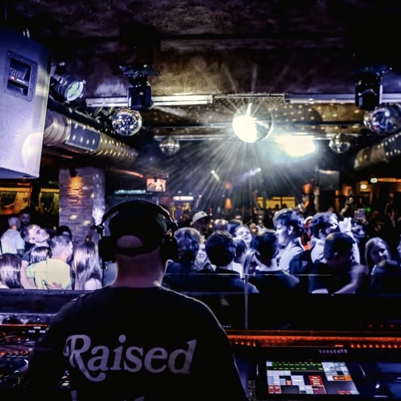 DJ Driessen an den Decks mit tanzender Menge auf der Tanzfläche, beleuchtet von bunten Lichtern und Diskokugel.