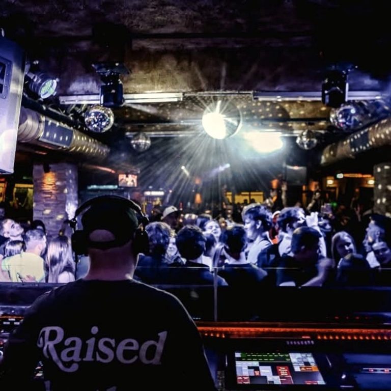 DJ Driessen spielt vor einer tanzenden Menge in einem beleuchteten Club.