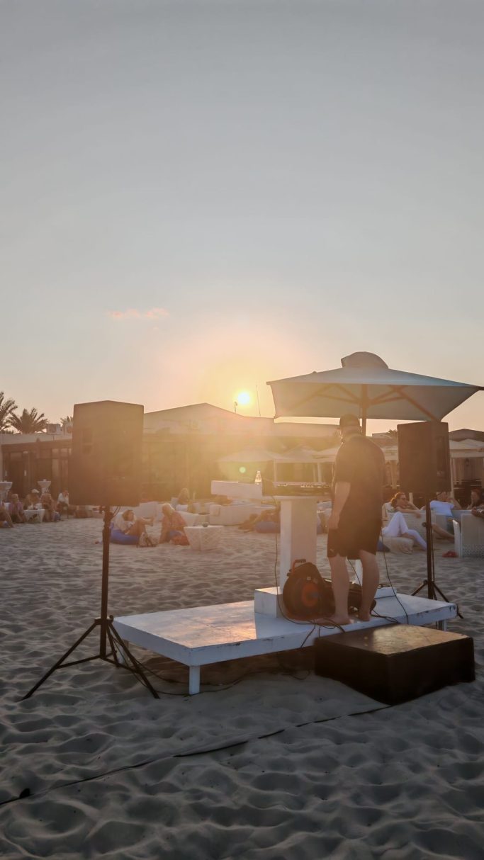 Sonnenuntergang am Strand mit Sonnenliege und Musiklautsprechern im Vordergrund.